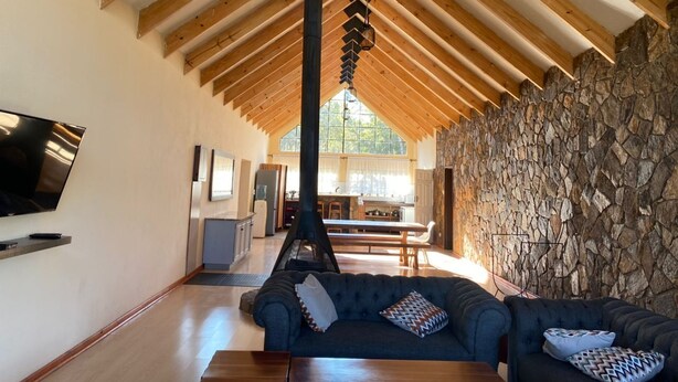 A spacious living area with a high ceiling, wooden beams, a stone wall, and a fireplace.