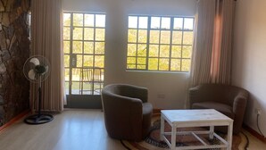 A room with a stone wall, two windows with curtains, a fan, two chairs, and a small table.