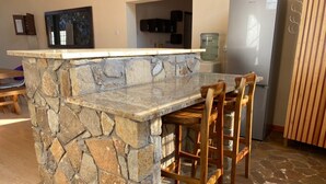 A kitchen with a stone island, wooden chairs, a refrigerator, and cabinets.