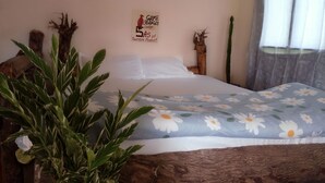 A bed with a floral bedspread, a wall-mounted sign, and a plant in the foreground. - natural environment from river side (ARUSHA)