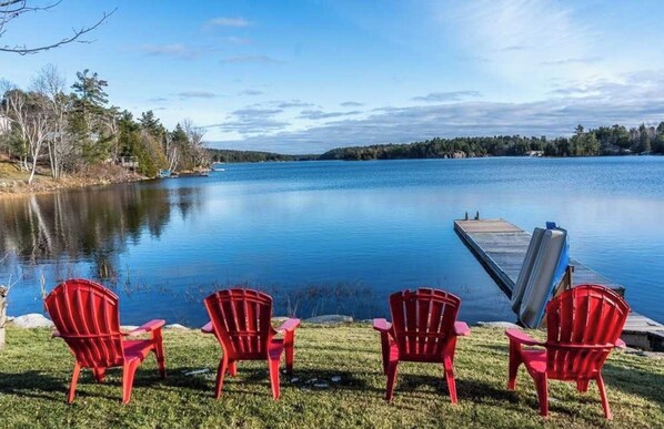 Relax on the lakeside with a serene view of the calm water, surrounded by lush trees and a wooden dock.
