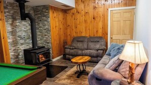 A cozy living room with a stone wall, wooden paneling, a sofa, a lamp, and a pool table. - Waterfront Cottage with HotTub! Next to OFSC trails (French River)