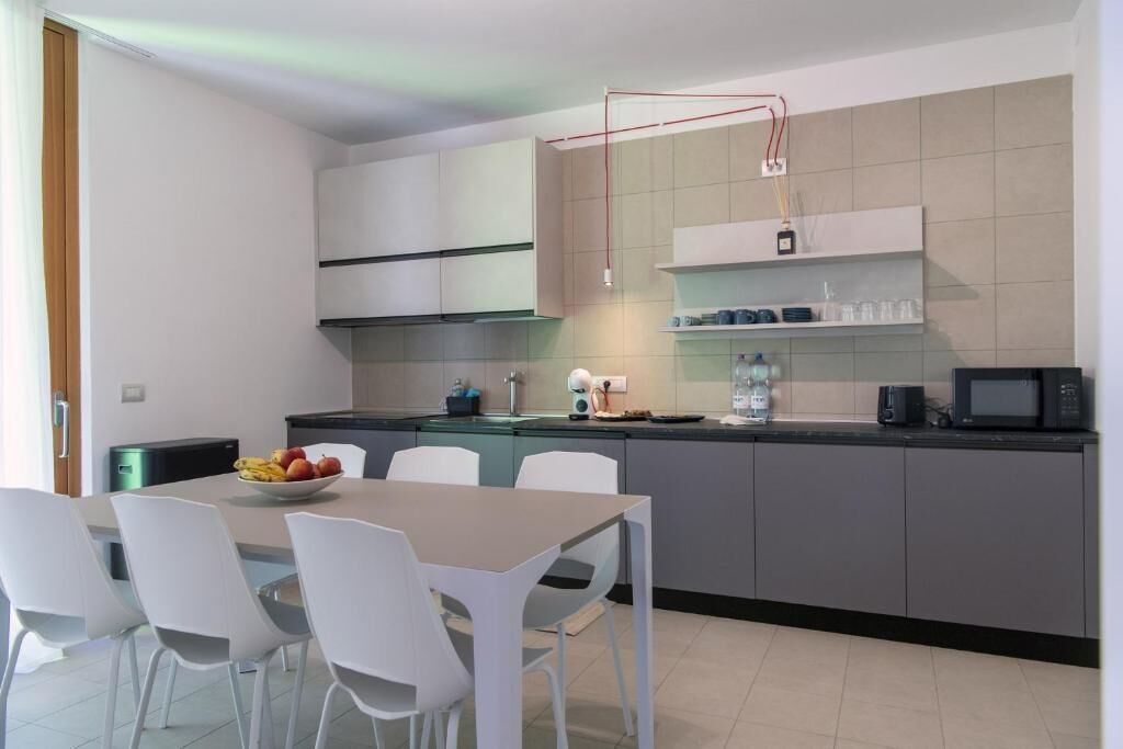 A modern kitchen with white cabinets, a dining table with chairs, and a fruit bowl.