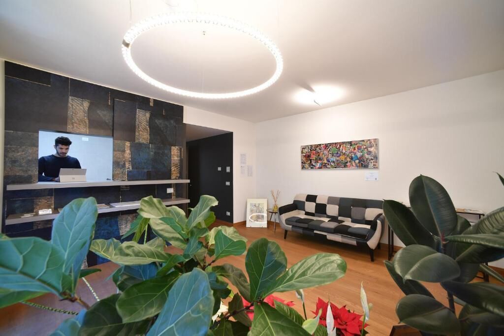 Un área de recepción moderna con una pantalla de televisión grande, un sofá a cuadros blanco y negro, y un cuadro abstracto colorido en la pared.