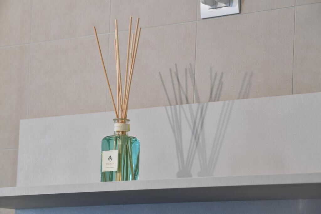 A bathroom with a white sink, a mirror, and a bottle of reed diffuser on the counter.