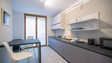 A modern kitchen with a dining area, featuring a dark countertop, white chairs, and a large window.