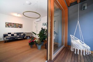 A modern living room with a sofa, potted plants, and a macrame hanging chair.