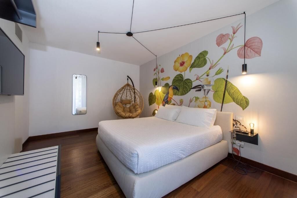 Un dormitorio moderno con una cama grande, una silla colgante, un televisor montado en la pared y un mural de flores.