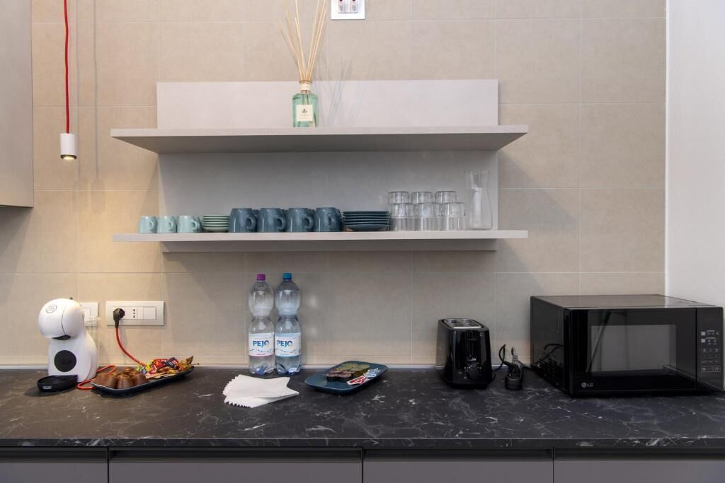Una cucina con un piano di lavoro nero, uno scaffale bianco con stoviglie, un forno a microonde, un tostapane e una macchina da caffè.