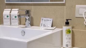 Un baño con lavamanos blanco, un espejo y una botella de jabón corporal.