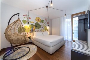 A modern bedroom with a bed, a hanging chair, a wall mural, and a TV.
