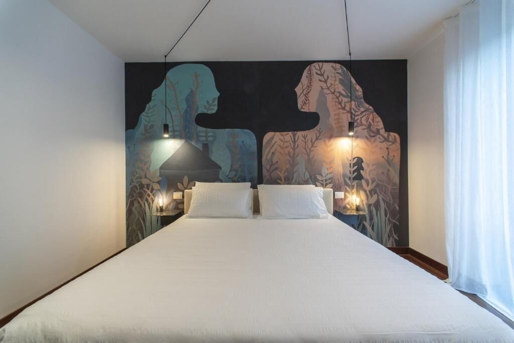 Un dormitori amb un llit gran, dues làmpades de nit i un mural a la paret.