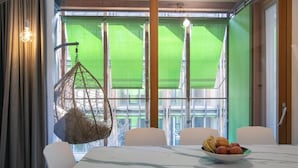 A dining area with a table set for two, a hanging chair, and a bowl of fruit on the table. - Habitat Apartments (Trento)