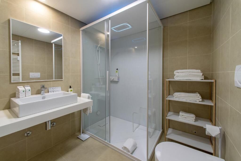 Une salle de bain moderne avec une douche à parois de verre, un lavabo blanc et une étagère intégrée où sont rangées les serviettes.