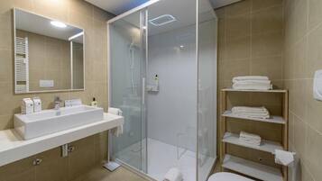 Une salle de bain moderne avec une douche à parois de verre, un lavabo blanc et une étagère intégrée où sont rangées les serviettes.