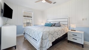 Un dormitorio con cama, mesita de noche, televisor y ventilador de techo.