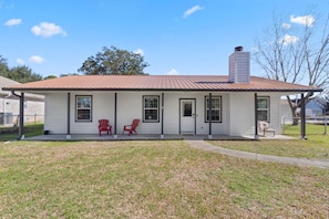 A single-story house with a metal roof, a chimney, and a front porch with two red Adirondack chairs.