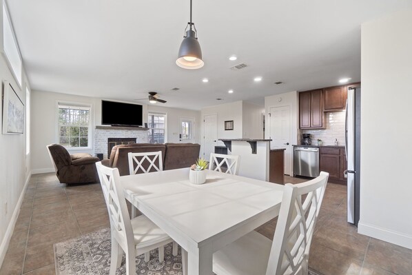 A modern kitchen with white cabinetry, a stainless steel refrigerator, and a dining area with a white table and chairs.