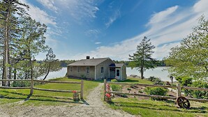 A rustic cabin by a lake with a clear path leading to the entrance, surrounded by greenery and a wooden fence. - Nest On Mount Desert Isle w Beach - 8 Mi to Acadia (Mt Desert)