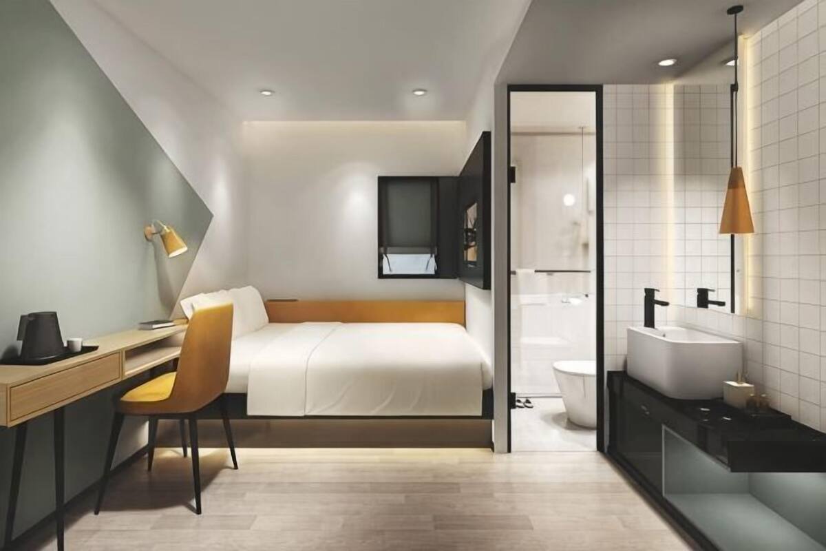 A modern hotel room with a bed, desk, chair, and a bathroom with a toilet and sink.