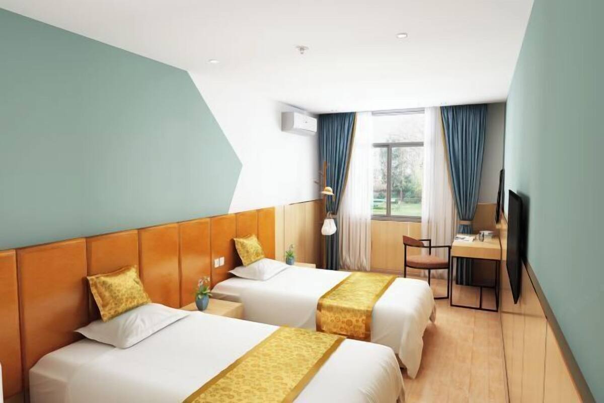 A hotel room with two beds, a desk, a chair, a TV, and a window with curtains.