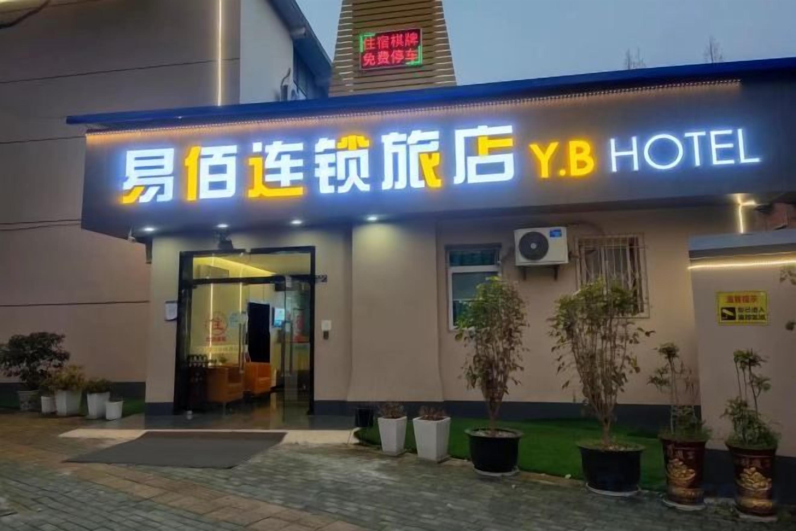 Ingresso di un hotel con insegna al neon, piante in vaso e condizionatore d'aria.
