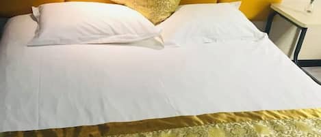 A neatly made bed with white linens and a patterned bedspread, a single decorative pillow, and a folded towel on the side.