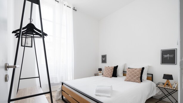 Un dormitorio moderno con estructura de cama de madera, ropa de cama blanca y una mesita de noche con lámpara.