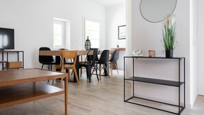 Un comedor moderno con una mesa y sillas de madera, una consola negra con un jarrón y un espejo grande en la pared.