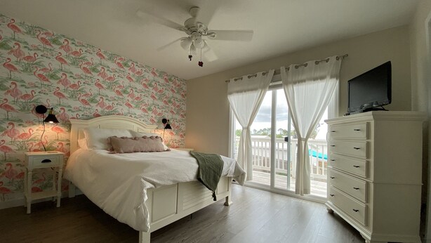 A bedroom with a bed, nightstands, a dresser, a ceiling fan, and a window with curtains. - Quaint Beach 2-Bedroom Townhome - less than 2 blocks to the ocean! (Port St. Joe)