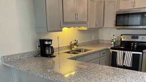 A kitchen with grey cabinets, a granite countertop, a coffee maker, a sink, and a stove. - Quaint Beach 2-Bedroom Townhome - less than 2 blocks to the ocean! (Port St. Joe)