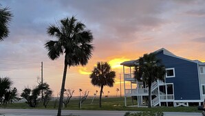 A coastal building with a blue exterior and a white balcony, surrounded by a wooden fence and palm trees. - Quaint Beach 2-Bedroom Townhome - less than 2 blocks to the ocean! (Port St. Joe)