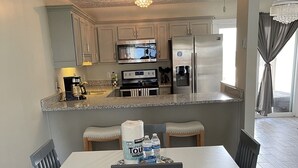A modern kitchen with stainless steel appliances, a dining area with a white table and chairs, and a ceiling fan. - Quaint Beach 2-Bedroom Townhome - less than 2 blocks to the ocean! (Port St. Joe)