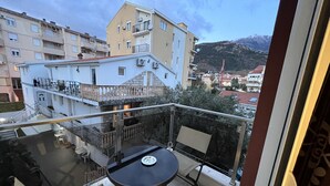 Un balcón con mesa y sillas, con vista a un paisaje urbano que incluye edificios y montañas.