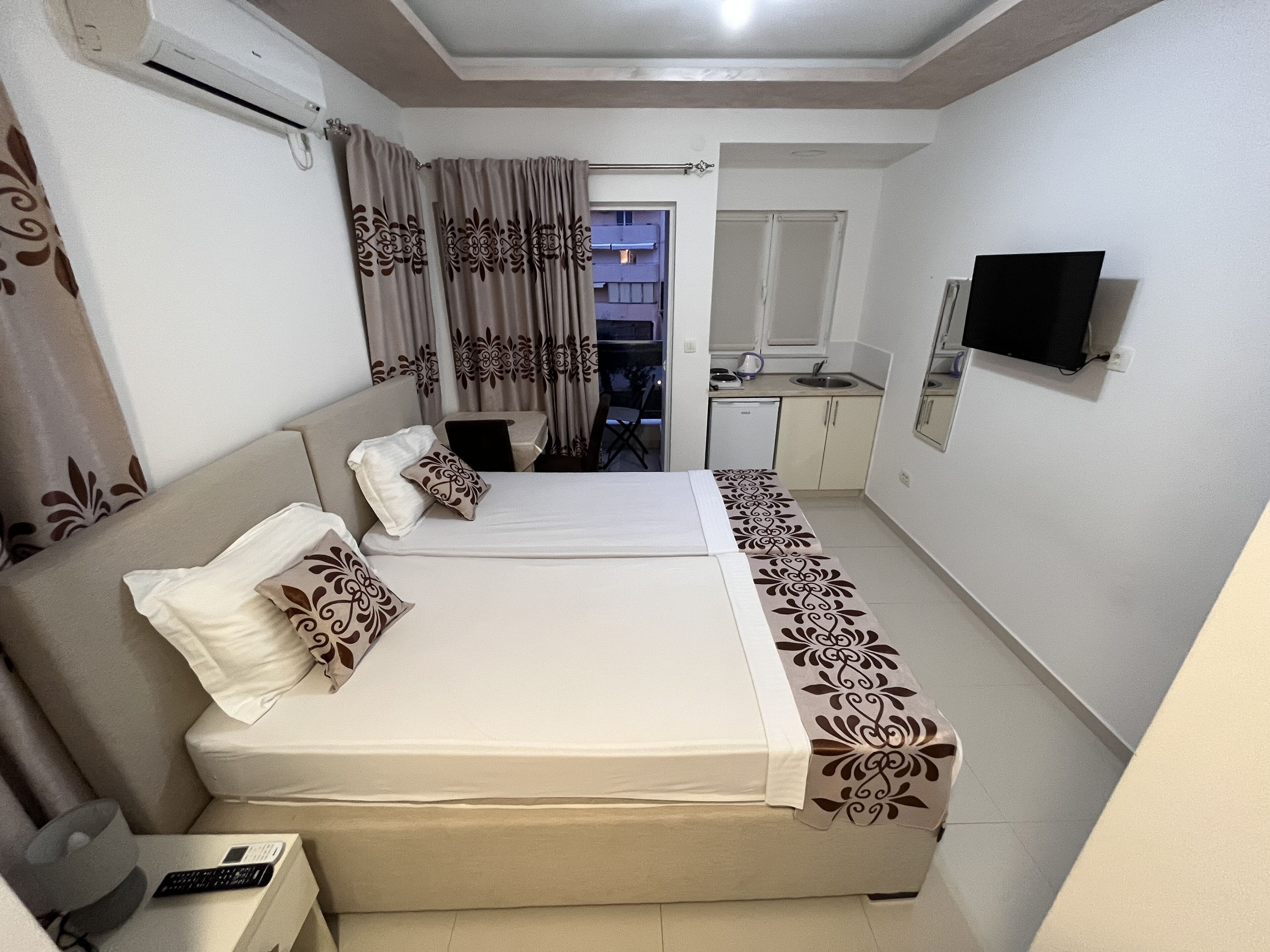 Een hotelkamer met een tweepersoonsbed, een klein bureau met stoel, een aan de muur bevestigde televisie en een kitchenette.