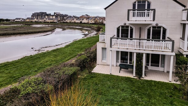 A two-story white house with a balcony, a river in the background, and a grassy area in the foreground. - AR MOR 603 - One Bedroom Apartment, Sleeps 4 (Courseulles-sur-Mer)