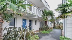 A narrow pathway flanked by lush greenery and a building with multiple doors and balconies. - AR MOR 603 - One Bedroom Apartment, Sleeps 4 (Courseulles-sur-Mer)