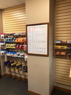 A snack aisle with labeled sections for drinks, fruit, snacks, and frozen treats. - The Lodge at Wisp Resort (McHenry)