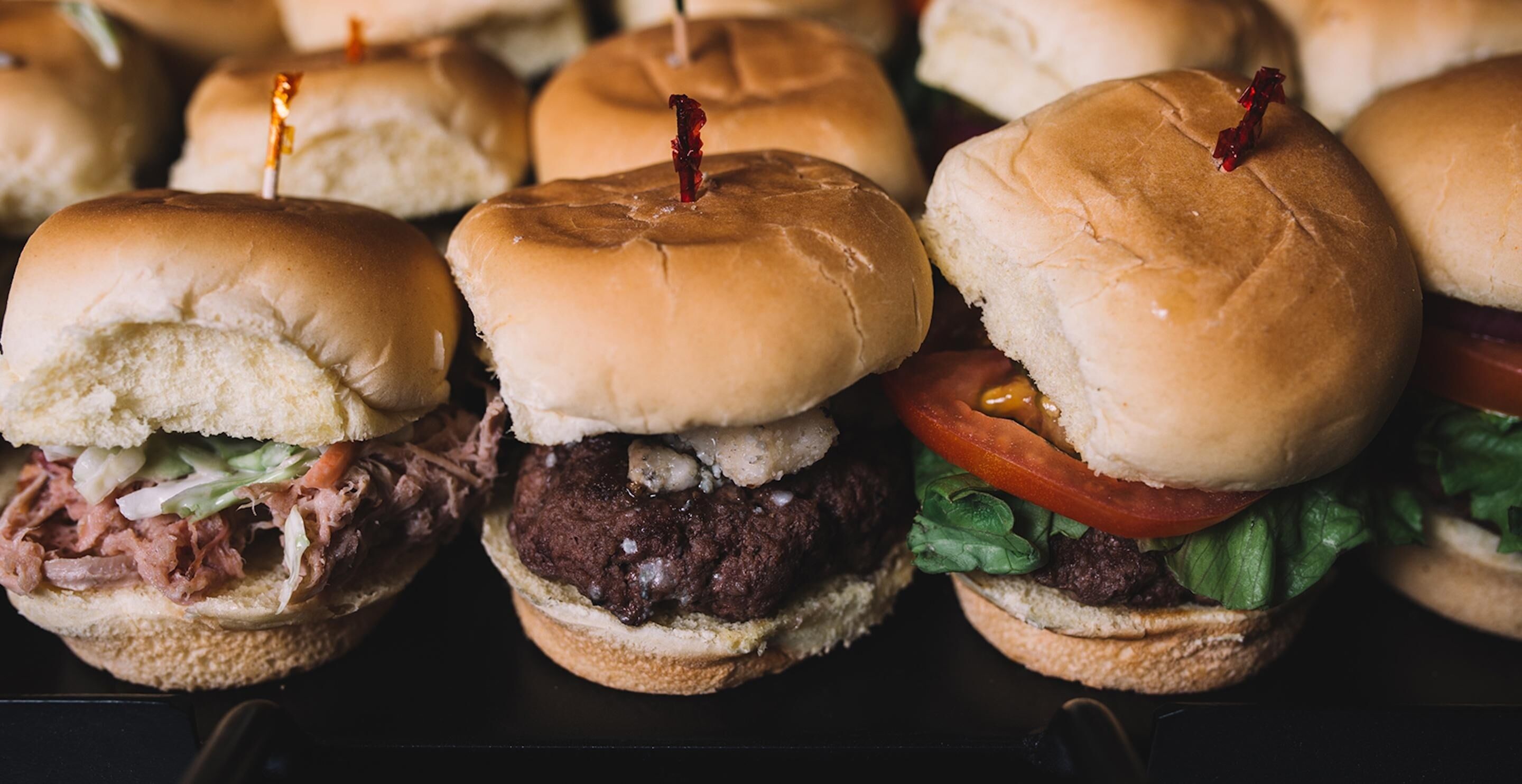 A row of sandwiches with buns, some with toothpicks.