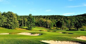 A golf course with sand bunkers, trees, and a clear sky.