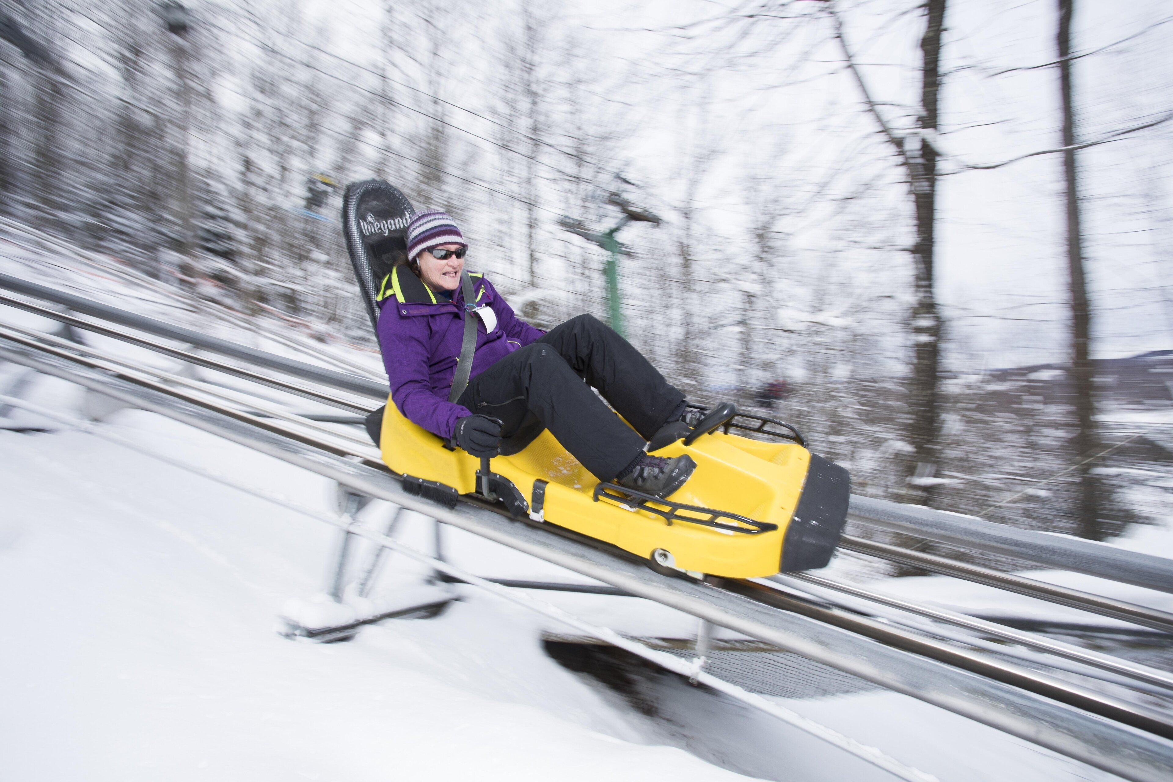 Une personne se déplace sur une sorte de luge le long d’une piste enneigée.