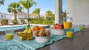 Een ontbijt met uitzicht op een zwembad, met fruit, muffins en sinaasappelsap.