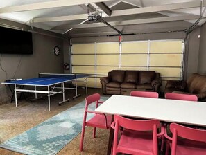 Una stanza con un tavolo da ping pong, un divano in pelle marrone e un tavolo bianco con sedie rosa.