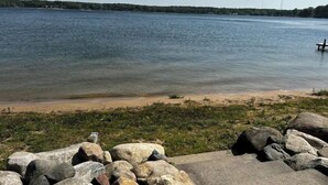 Un lac paisible, avec une plage de sable et de gros rochers au premier plan.