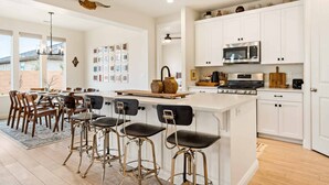Een moderne keuken met witte kasten, een centraal eiland met barstoelen, een magnetron en een fornuis.