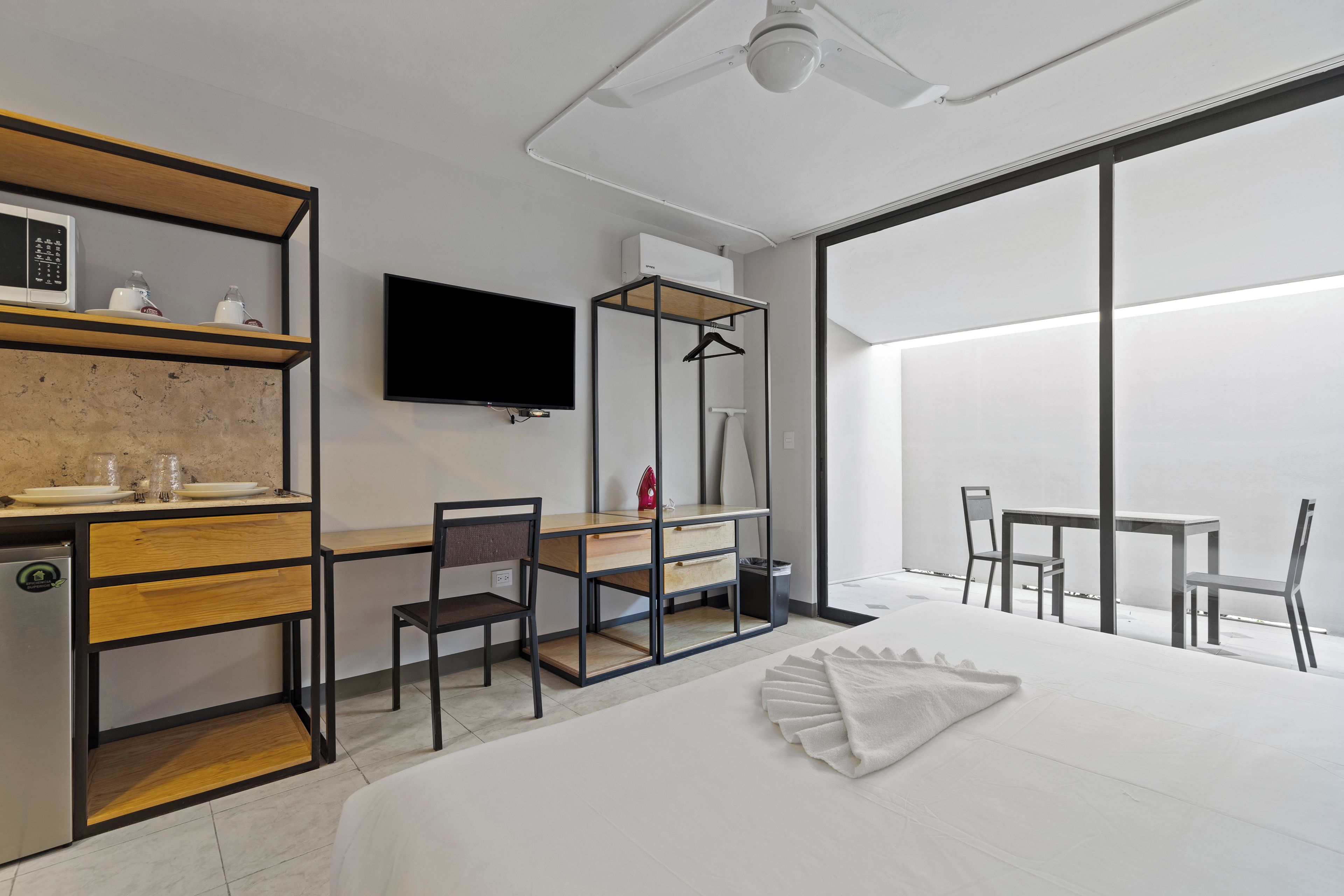 A modern hotel room with a bed, a desk, a chair, a TV, and a large window.
