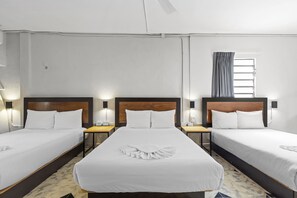 Three single beds with wooden headboards and white bedding, set in a simple, functional room with a small table and nightstands.