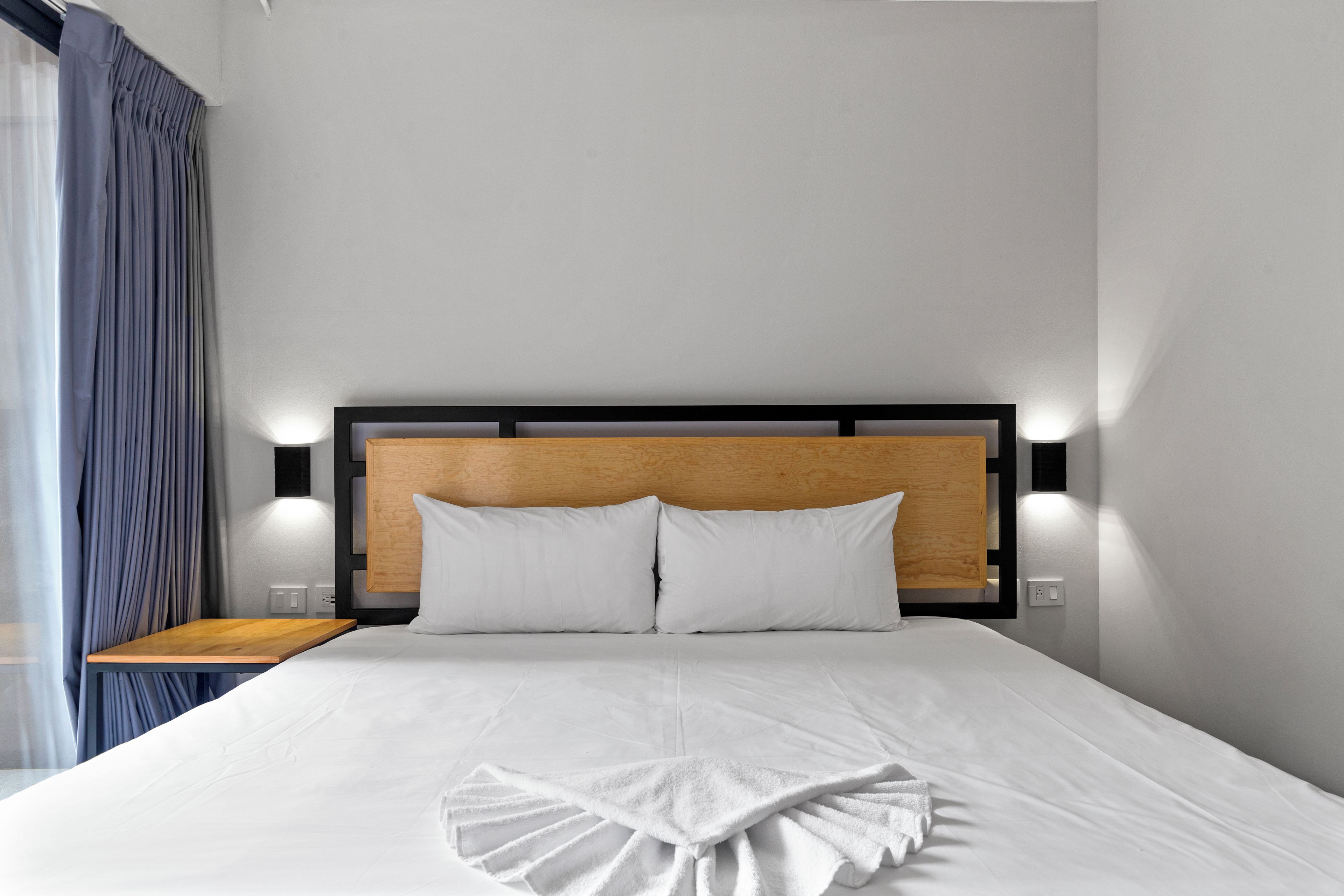 Une chambre d’hôtel avec un lit bien fait, une tête de lit en bois et une table de chevet avec une lampe.