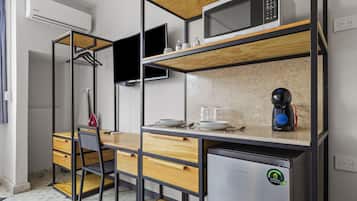 A compact kitchenette with a microwave, coffee maker, and a refrigerator. There is a wooden table with a chair and a TV mounted on the wall.