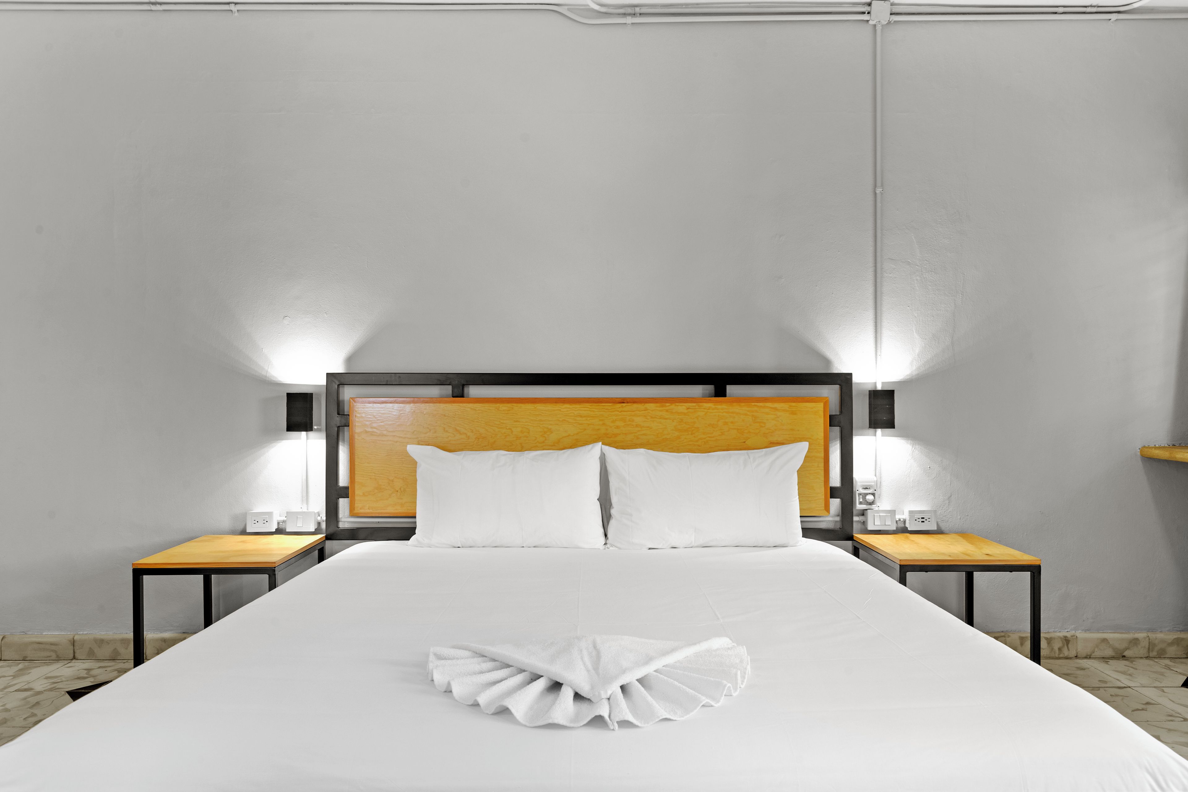 A hotel room with a large bed, two bedside tables, a wooden headboard, and two wall-mounted lamps.